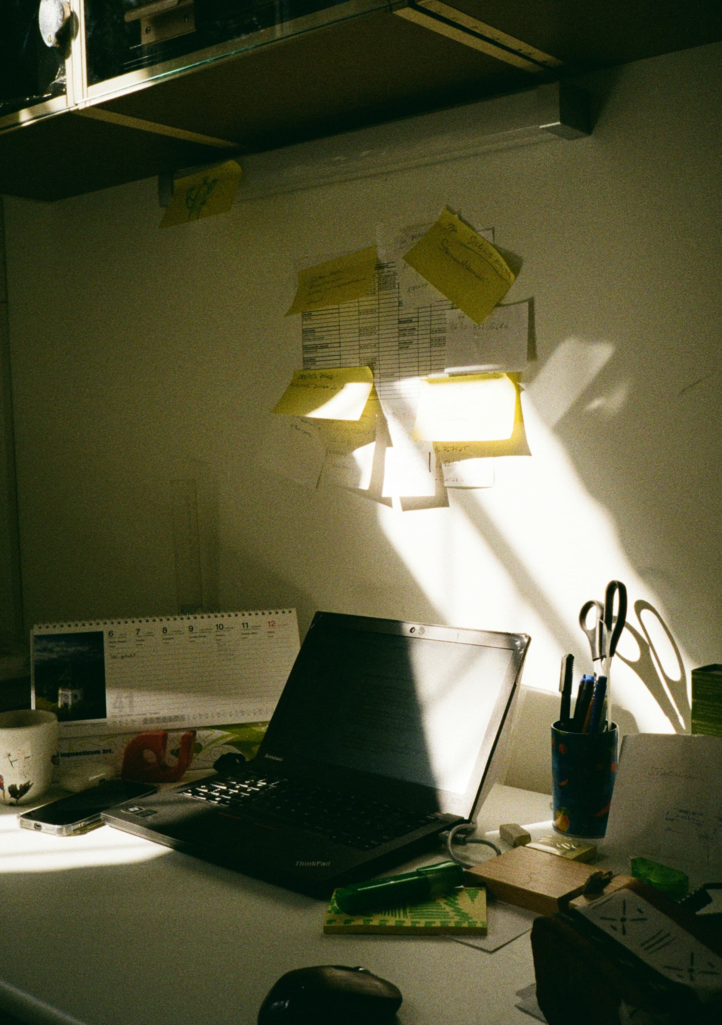 A naturally lit desk with a laptop, calendar, notes, and reminders